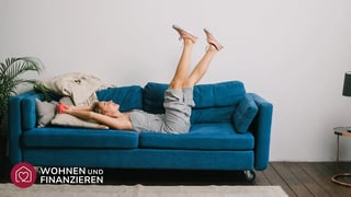Frau hat Eigentumswohnung gekauft und liegt glücklich auf ihrer Couch