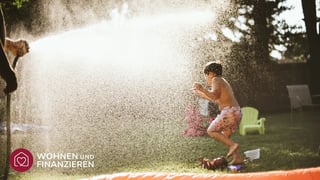 Kind spielt im Garten mit Rasensprenger